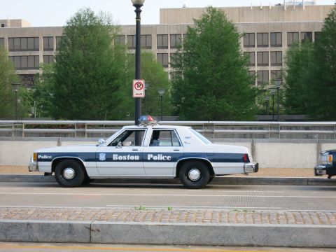 1991 Ford LTD Crown Victoria - Side view of a white-and-blue Boston Police sedan parked on a bridge near a lamppost and city buildings.