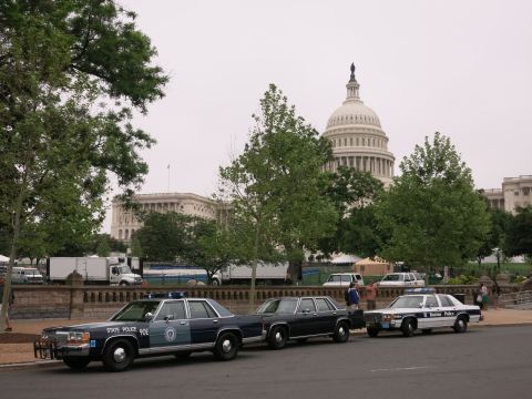 1991 Ford LTD Crown Victoria - navy State Police sedan with push bar leads a line of sedans on a street with the U.S. Capitol dome in the background.