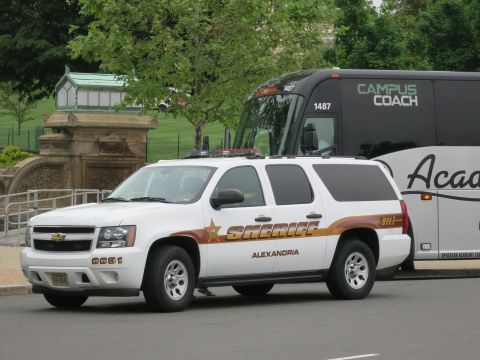 1991 Ford LTD Crown Victoria - white Chevrolet Suburban marked Sheriff Alexandria sits in front of a black-and-white Campus Coach motorcoach.