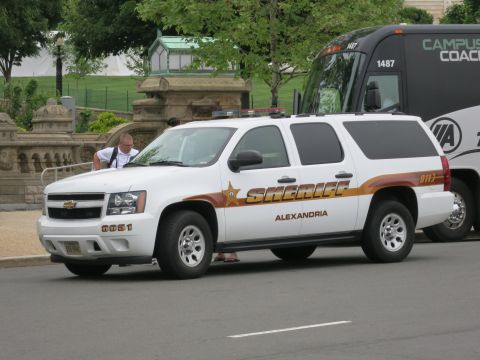 1991 Ford LTD Crown Victoria - white Chevrolet Suburban marked Sheriff Alexandria is parked by a coach bus while a person stands at its front.