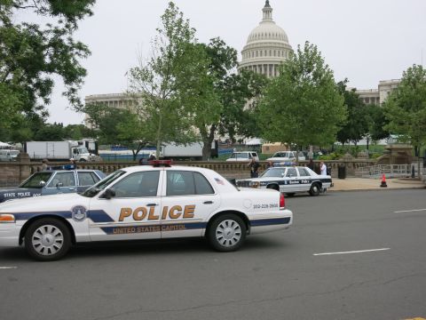 1991 Ford LTD Crown Victoria - white United States Capitol Police cruiser sits at an intersection with the U.S. Capitol dome rising behind trees.