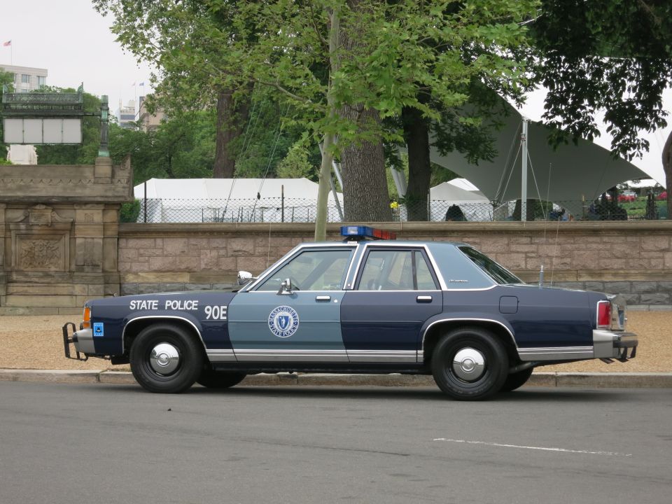 Profile of navy and gray State Police sedan #90E parked at curb