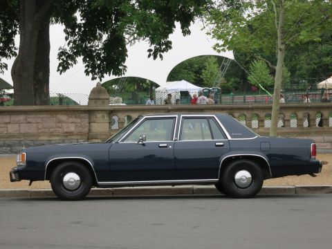 1991 Ford LTD Crown Victoria - dark blue full-size sedan with chrome trim and steel-hubcap wheels is parked in profile beside a stone balustrade.