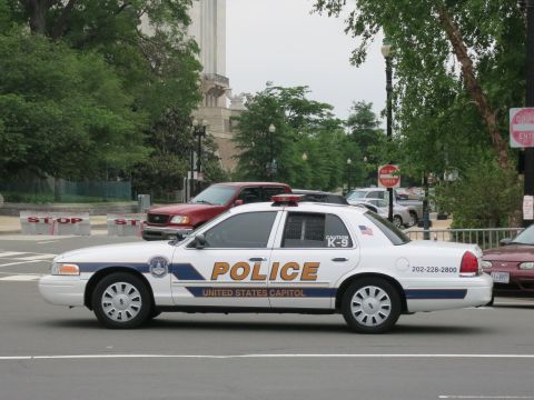 1991 Ford LTD Crown Victoria - white United States Capitol Police K-9 cruiser sits in side profile near stop barriers and a red pickup on a city street.