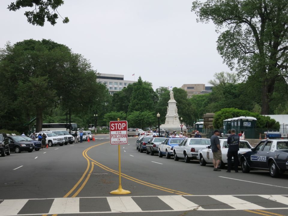 Street view of parked cars and a stop sign near a statue and monument