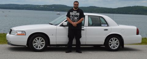 2000 Mercury Grand Marquis - A white sedan is parked next to a body of water with a man standing in front of it.