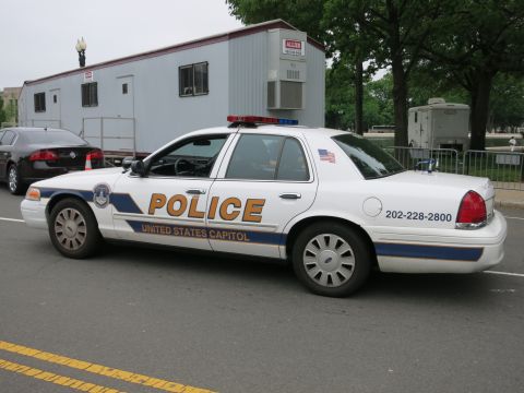 1991 Ford LTD Crown Victoria - white and blue United States Capitol Police sedan with phone number 202-228-2800 parked along a curb beside a trailer.