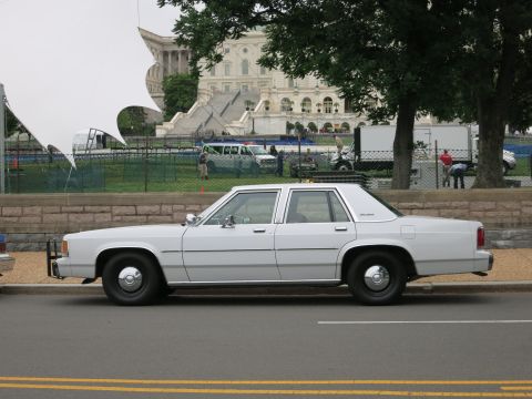 1991 Ford LTD Crown Victoria - plain white four-door sedan parked along a curb with the U.S. Capitol building visible in the background.