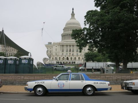 1991 Ford LTD Crown Victoria - blue and white police sedan marked POLICE 334-2424 parked in front of the U.S. Capitol dome and portable toilets.