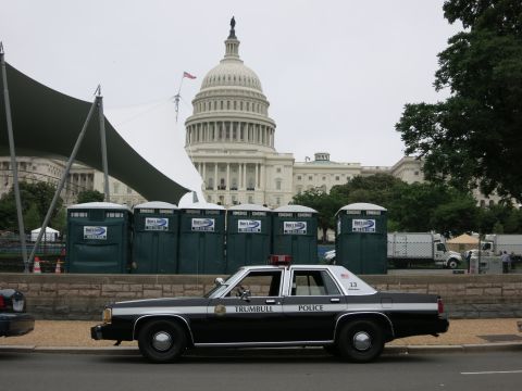 1991 Ford LTD Crown Victoria - black and white Trumbull Police sedan parked in front of green portable toilets with the U.S. Capitol dome behind.