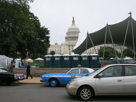 1991 Ford LTD Crown Victoria - blue Police sedan and a silver hatchback parked near green portable toilets in front of the U.S. Capitol dome.
