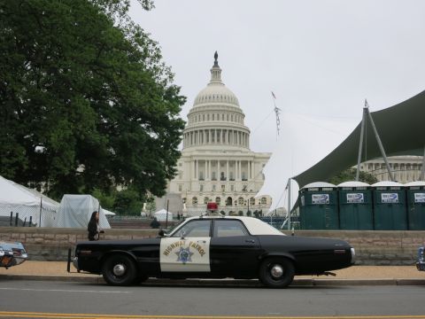 1991 Ford LTD Crown Victoria - black and white Highway Patrol car with red roof light parked along a curb in front of the U.S. Capitol and tents.