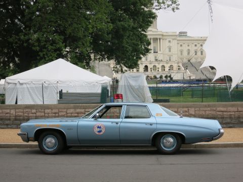 1991 Ford LTD Crown Victoria - light blue police sedan with red roof light parked along a curb in front of white tents near the U.S. Capitol.