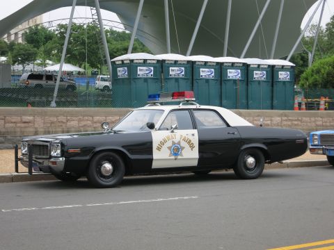 1991 Ford LTD Crown Victoria - black-and-white classic full-size police sedan marked California Highway Patrol parked along a curb near a tented venue.