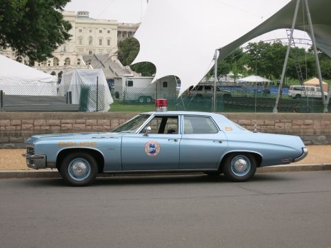 1991 Ford LTD Crown Victoria - light-blue 1970s full-size four-door police sedan lettered POLICE with a circular department emblem, parked near a domed building.