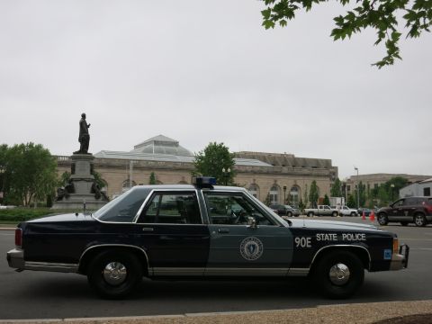 1991 Ford LTD Crown Victoria - dark-blue Ford full-size State Police sedan numbered 90E parked in front of a stone building with a statue.