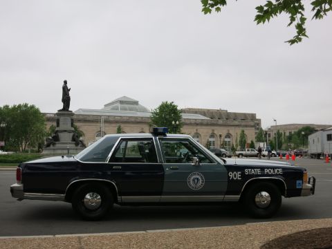 1991 Ford LTD Crown Victoria - dark-blue Ford full-size State Police sedan marked 90E parked before a domed stone building with a statue.