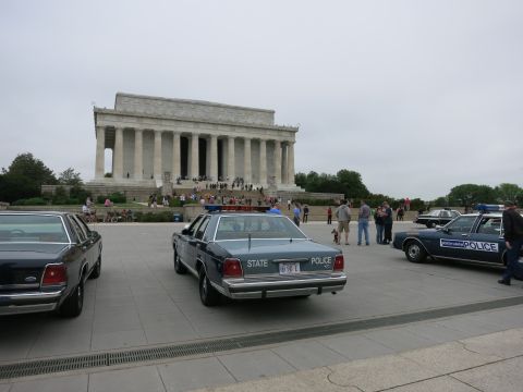 1991 Ford LTD Crown Victoria - blue STATE POLICE sedan and other police cars parked in front of the Lincoln Memorial as visitors gather on the steps.