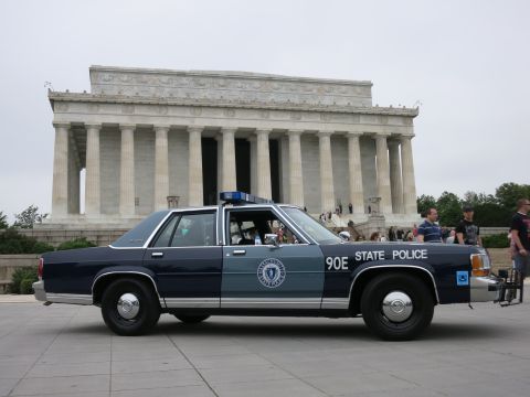 1991 Ford LTD Crown Victoria - two-tone navy and silver Ford police sedan marked "90E State Police" sits before the columned Lincoln Memorial as tourists gather on the st…
