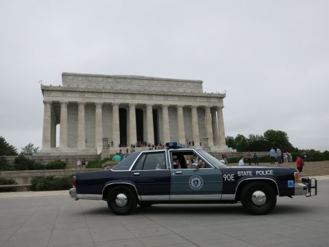 1991 Ford LTD Crown Victoria - two-tone navy and gray "90E State Police" Ford sedan parked on a plaza with the Lincoln Memorial and crowds in the background.
