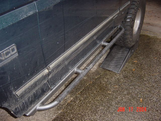 Tube rock-slider step bar mounted along the rocker of a dark Bronco on pavement