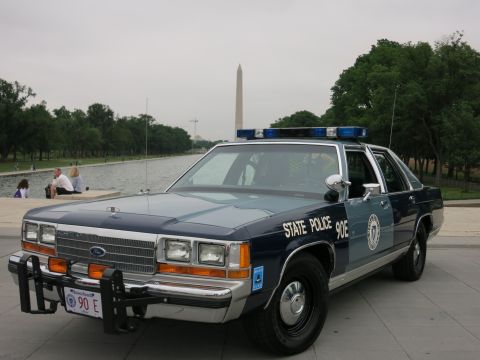 1991 Ford LTD Crown Victoria - navy and silver "State Police 90E" Ford cruiser with push bar, photographed head-on with the Washington Monument reflected in the pool behi…