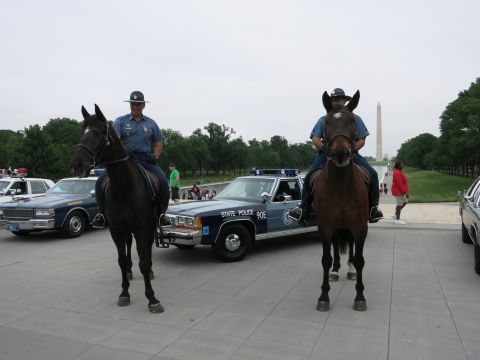 1991 Ford LTD Crown Victoria - Two police officers in campaign hats sit on horseback flanking a navy "90E State Police" Ford cruiser, with the Washington Monument behind.