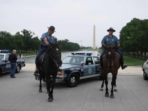 1991 Ford LTD Crown Victoria - Two mounted police officers in campaign hats flank a navy "State Police 90E" Ford cruiser, the Washington Monument visible across the Refle…