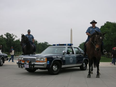1991 Ford LTD Crown Victoria - Two officers in campaign hats on horseback flank a navy "State Police 90E" Ford cruiser with push bar, the Washington Monument centered beh…