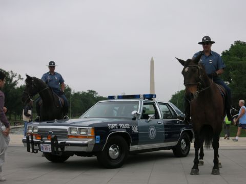 1991 Ford LTD Crown Victoria - Two officers on horseback in dress uniforms flank a navy "State Police 90E" Ford cruiser, the Washington Monument behind under an overcast…