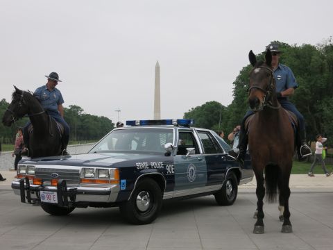 1991 Ford LTD Crown Victoria - Two officers in campaign hats on horseback flank a navy "State Police 90E" Ford cruiser, the Washington Monument and Reflecting Pool behind.