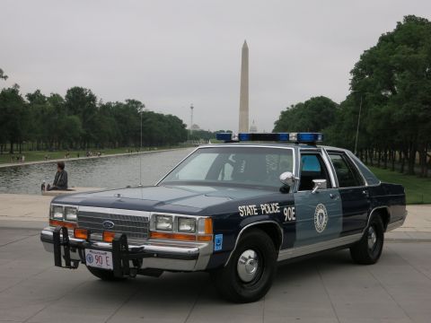 1991 Ford LTD Crown Victoria - vintage blue-and-silver 'State Police 90E' Ford sedan with a push bar and roof lightbar parked beside the reflecting pool with the Washingt…
