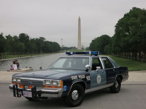 1991 Ford LTD Crown Victoria - blue-and-silver 'State Police 90E' Ford patrol car parked on the plaza beside the reflecting pool with the Washington Monument and people b…