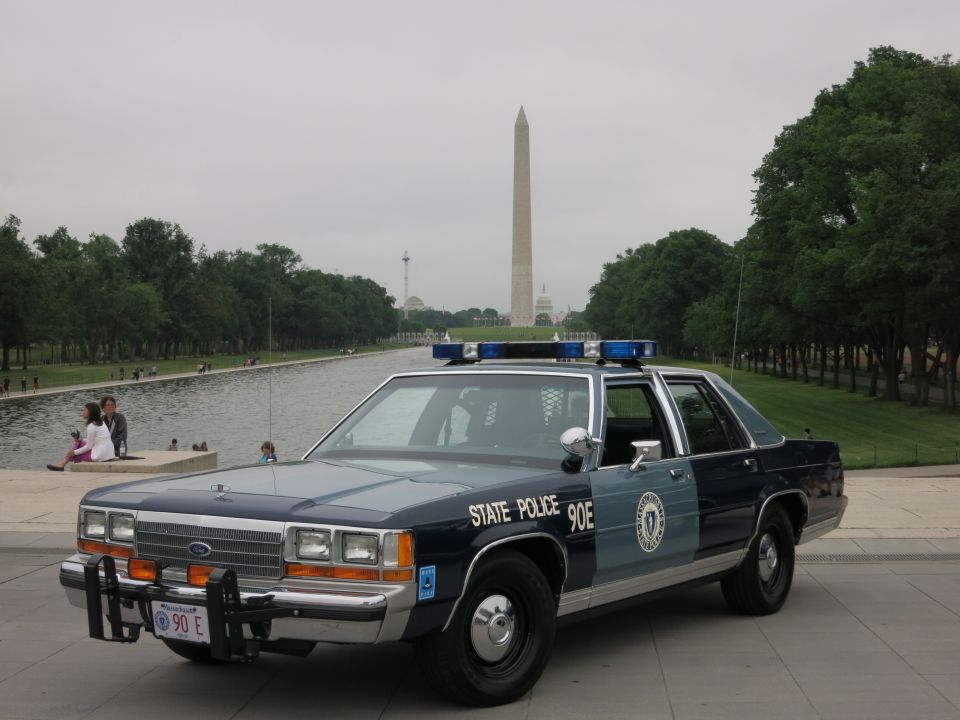 Blue and silver State Police Ford sedan at reflecting pool, monument behind