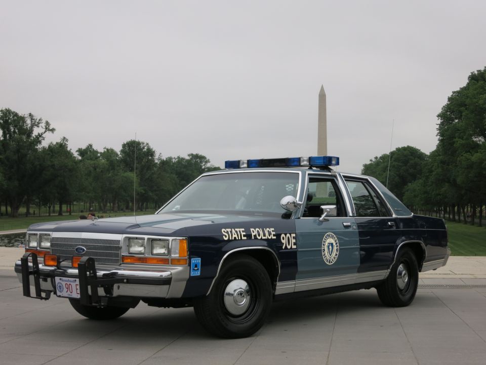 Blue and silver State Police Ford sedan on grass with Washington Monument behind
