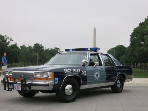 1991 Ford LTD Crown Victoria - blue-and-silver 'State Police 90E' Ford patrol sedan with push bar parked on pavement, a man standing nearby and the Washington Monument be…