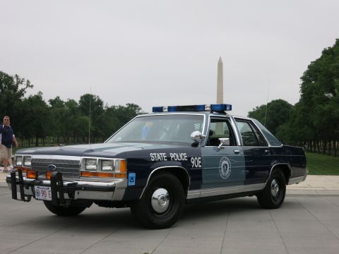 1991 Ford LTD Crown Victoria - Front three-quarter view of a blue-and-silver 'State Police 90E' Ford patrol sedan with push bar and lightbar, the Washington Monument dire…