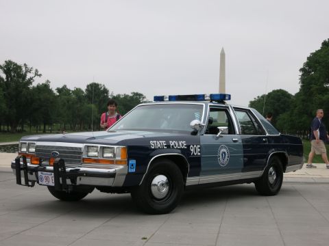 1991 Ford LTD Crown Victoria - blue-and-silver 'State Police 90E' Ford patrol sedan parked on a plaza with several pedestrians around it and the Washington Monument behin…