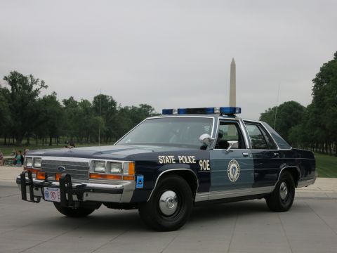 1991 Ford LTD Crown Victoria - blue-and-silver 'State Police 90E' Ford patrol sedan with push bar and roof lightbar parked on pavement, trees and the Washington Monument…