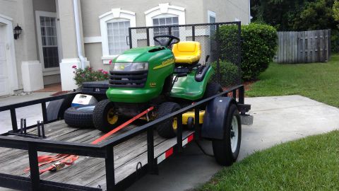 1994 Ford Bronco - A green and yellow John Deere L100 lawn tractor is secured to a trailer with a cooler and spare tire.