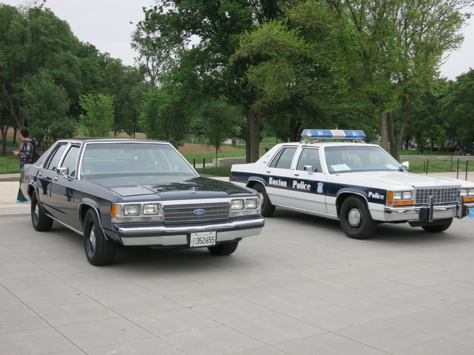 Black civilian Ford sedan and white Boston Police Ford sedan on plaza