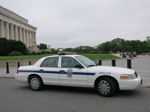 1991 Ford LTD Crown Victoria - Side view of a white Ford Crown Victoria police sedan with blue stripe and roof lightbar parked before the Lincoln Memorial colonnade.