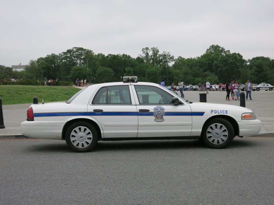 White Crown Victoria police car side profile with blue stripe, park behind