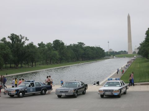 1991 Ford LTD Crown Victoria - Three vintage Ford sedans, including a State Police car and a black sedan, parked beside the reflecting pool with the Washington Monument b…