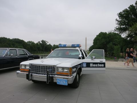 1991 Ford LTD Crown Victoria - white and blue Boston Police Ford sedan with its driver door open is parked on a plaza with the Washington Monument in the distance.