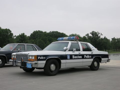 1991 Ford LTD Crown Victoria - white and dark blue Boston Police Ford sedan with light bar is parked on a stone plaza beside another cruiser.