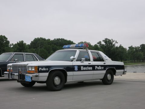1991 Ford LTD Crown Victoria - white-over-blue Boston Police Ford sedan with roof light bar is parked on a plaza next to a similar cruiser.