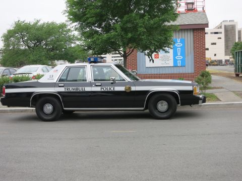 1991 Ford LTD Crown Victoria - black and white Trumbull Police Ford sedan with unit number 13 is parked curbside in front of a brick building.