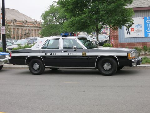 1991 Ford LTD Crown Victoria - black-over-white Trumbull Police Ford sedan, unit 13, is parked along a street near brick buildings and a Water Street sign.