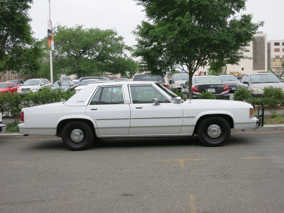 Plain white Ford LTD Crown Victoria sedan parked in lot, side view